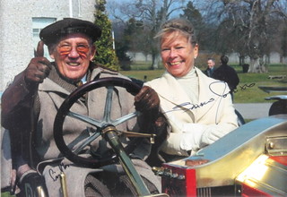 Sir Stirling Moss and Sue Moss, a coloured photograph of the couple seated in a vintage motorcar outside Goodwood House 8" x 11" 