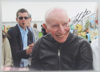 John Surtees, a signed colour photograph of John Surtees wearing a black leather motorcycle jacket 