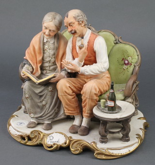 A signed Capodimonte group Ricordi of an elderly lady and gentleman sitting on a couch looking at a photograph album signed Volta 11" 