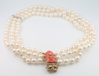 A 3 strand cultured pearl necklace with white gold and diamond set bars, the yellow gold clasp diamond set and with a carved coral portrait mask 