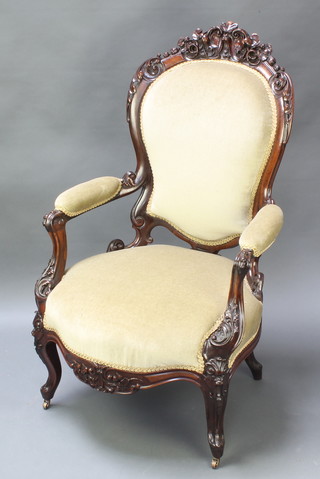 A Victorian heavily carved mahogany show frame open arm chair upholstered in green Dralon raised on carved cabriole supports 