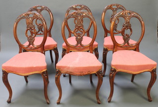 A set of 6 Victorian carved walnut balloon back dining chairs with pierced vase shaped slat backs, the seats of serpentine outline upholstered in pink material 