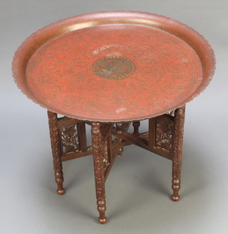 A Benares brass table raised on a carved hardwood folding stand decorated a peacock 19" x 23" diam. 