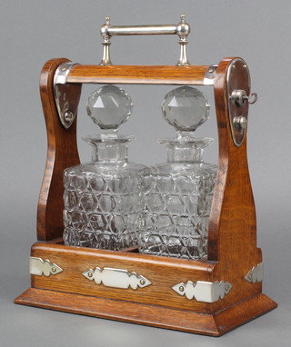 An Edwardian silver plated mounted oak 2 bottle tantalus with square cut decanters 