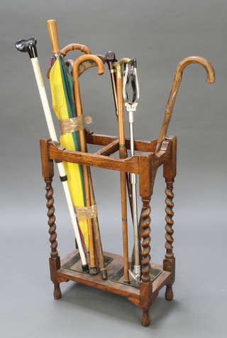 An oak twin division umbrella stand with metal drip trays, raised on barley twist supports containing a shooting stick and a collection of walking sticks 27 1/2" x 18" x 9" 