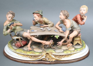 A large Capodimonte group of children playing cards at a table, signed Merlic 22" 