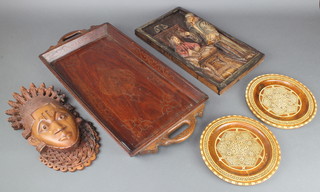 An Indian hardwood and inlaid brass twin handled tray 19", a carved and pierced hardwood mask, a rectangular carved oak panel of an interior scene with figures 15" x 8", 2 circular inlaid chargers 7 1/2" 