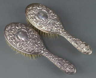 A pair of repousse silver hair brushes with masks, scrolls and birds 