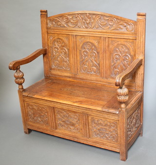 An Edwardian carved light oak settle with arched carved panelled back, the seat with hinged lid 45"h x 42"w x 20"d  