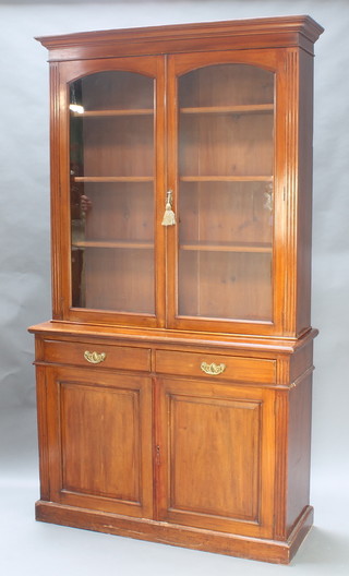 A Victorian bleached mahogany bookcase on cabinet with moulded cornice, fitted adjustable shelves enclosed by  arch shaped glazed doors having fluted columns to the sides, the base fitted 2 drawers above a double cupboard, raised on a platform base 87"h x 47 1/2"w x 17"d 