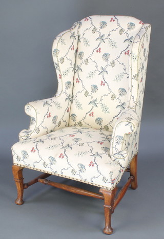 A Georgian style winged armchair upholstered in tapestry material, raised on cabriole supports with H framed stretcher 