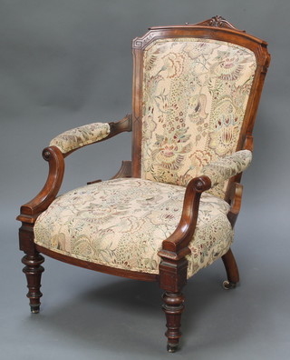 A Victorian carved mahogany show frame open arm chair upholstered in tapestry material raised on turned supports 