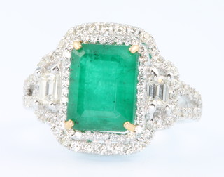 An 18ct white gold emerald and diamond cluster ring, the centre stone 3.1ct surrounded by brilliant and baguette cut diamonds 0.73ct, size K 1/2