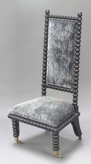 A Victorian ebonised and bobbin turned nursing chair with upholstered seat and back raised on turned supports 