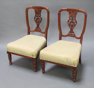 A pair of Victorian carved walnut nursing chairs with pierced vase shaped slat backs, raised on turned supports 