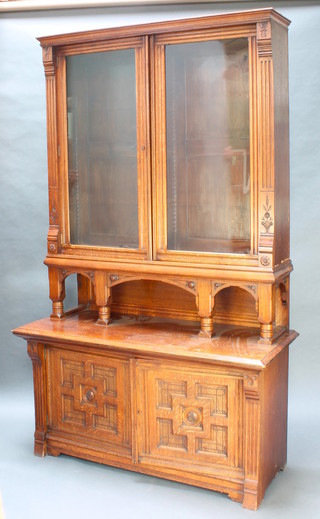 A Victorian oak aesthetic movement bookcase on cabinet, the upper section with moulded cornice, fitted adjustable shelves enclosed by glazed panelled doors, the base with arched recess above a cupboard enclosed by panelled doors 93 1/2"h x 56"w x 24"d Please note: The upper section is fitted to the base upside down