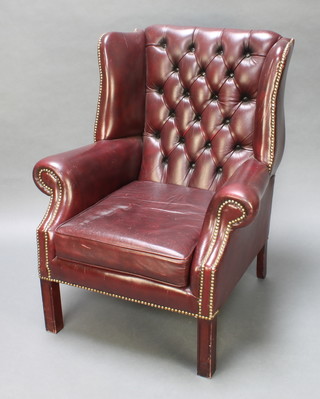 A Georgian style winged armchair upholstered in red buttoned leather on square supports