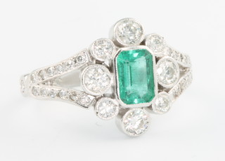 An 18ct white gold open shank Edwardian style emerald and diamond ring, the baguette cut emerald 0.7ct surrounded by brilliant cut diamonds 0.8ct, size N 