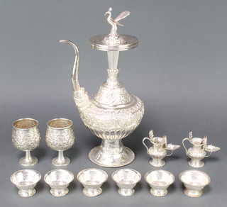 A Persian repousse silver ewer with peacock finial, 2 goblets, 6 table salts and 2 jugs in the form of oil lamps, 1628 grams 