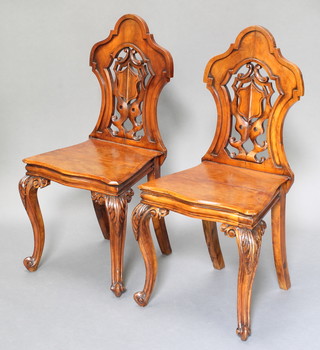 A pair of Victorian mahogany hall chairs with pierced backs and solid seats raised on cabriole supports 