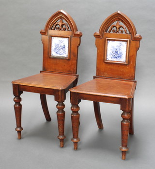A pair of Victorian mahogany hall chairs with solid seats and backs, the pierced backs inset blue and white tiles and raised on turned supports 