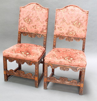 A pair of Carolean style oak framed high back chairs with upholstered seats and backs, raised on square supports with carved apron 