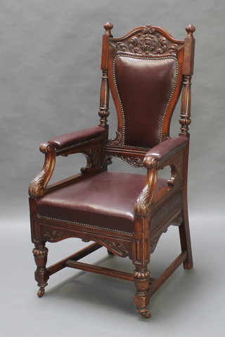 A Victorian carved mahogany open arm chair, the crest heavily carved, the seat and back upholstered in brown leather and raised on turned supports