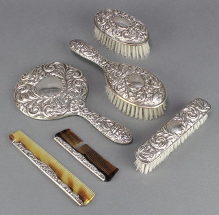 A silver repousse dressing table set comprising hand mirror, clothes brush, 2 hair brushes and 2 combs Birmingham 1976
