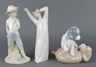 A Nao figure of a boy standing beside a trunk 9", a group of 2 puppies 5 1/2" and a yawning child 8" 