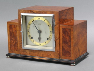 An Art Deco 8 day striking mantel clock, the square silvered dial with gilt chapter ring contained in a stepped figured walnut case  