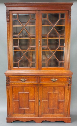 An Edwardian Art Nouveau bookcase on cabinet the upper section with moulded cornice, fitted shelves enclosed by astragal and bevelled glass panelled doors, the base fitted 2 long drawers above a double cupboard enclosed by panelled doors, raised on a platform base 86"h x 47 1/2"h x 18"d 