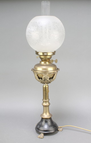 A Victorian brass oil lamp reservoir raised on a pierced brass stand with circular iron spreading foot and paw feet, having at etched glass shade and clear glass chimney converted for use as an electric table lamp  