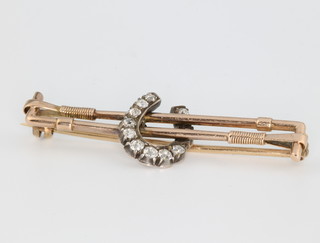 A yellow gold diamond set bar brooch in the form of a 2 riding crops and a horse shoe of brilliant cut diamonds 