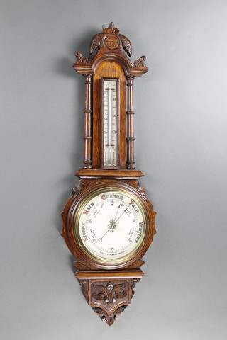 A Victorian aneroid barometer and thermometer contained in a carved oak wheel case with porcelain dial 