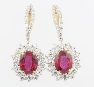 A pair of white gold oval ruby and diamond ear drops, the oval treated stones approx. 4.56ct surrounded by brilliant cut diamonds approx 1.78ct