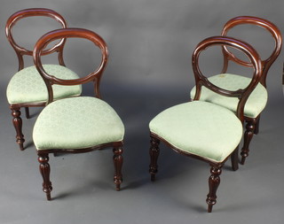 A set of 4 Victorian balloon back dining chairs with shaped mid rails and over stuffed seats, raised on turned and reeded supports