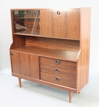 A stylish 1960's rosewood finished wall unit fitted display cabinet enclosed by glazed sliding doors flanked by a cocktail unit with fall front above a recess the base fitted 3 drawers and a cupboard 51 1/2"h x 48"w x 16"d 
