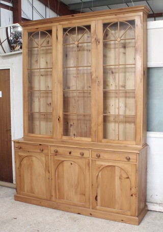 A Georgian style pine cabinet on cabinet, the upper section with moulded cornice fitted triple cupboards enclosed by arch shaped astragal glazed panelled doors, the base fitted 3 long drawers above a triple cupboard, raised on a platform base (no shelves to the upper section) 103 1/2"h x 73 1/2"w x 17 1/2"d 
