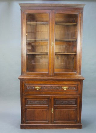 A late Victorian carved oak secretaire bookcase, the upper section with moulded cornice fitted adjustable shelves enclosed by glazed panelled doors, the base fitted a secretaire drawer above a double cupboard enclosed by panelled doors, raised on a platform base 93"h x 48"w x 19"d 
