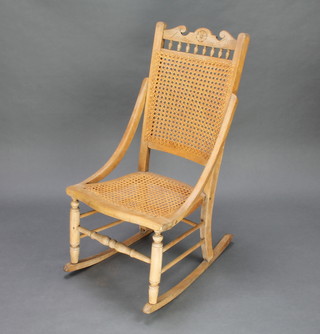An Edwardian carved bleached oak rocking chair with woven cane seat and back and bobbin turned decoration 