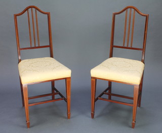 A pair of Edwardian inlaid mahogany stick and rail back bedroom chairs with double H frame stretcher raised on square tapering supports ending in spade feet