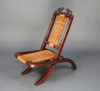 An Indian carved hardwood folding chair with woven cane seat and back decorated elephants