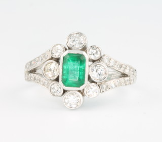 An 18ct white gold Edwardian style emerald and diamond ring, the centre baguette cut emerald surrounded by diamonds size M 