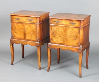 A pair of Queen Anne style figured walnut bedside cabinets with crossbanded tops, fitted a drawer above cupboard, raised on cabriole supports 71cm h x 44cm w x 13cm d 