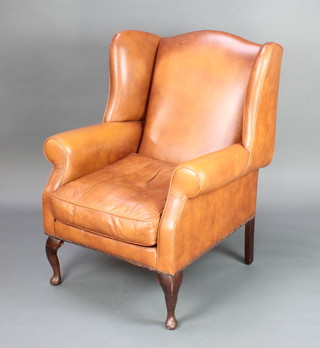 A Georgian style winged armchair upholstered in brown leather, raised on cabriole supports 102cm h x 80cm w x 69cm d 