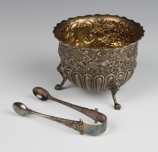An Edwardian repousse silver sugar bowl with demi-fluted and floral decoration on paw feet, together with a pair of ensuite sugar tongs London 1907, maker James Wakely & Frank Wheeler, 148 grams 