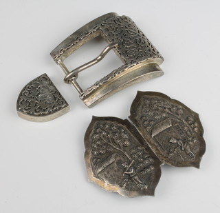 A sterling silver buckle with cast scroll decoration, a repousse silver ditto with figures before buildings in a jungle setting 265 grams 