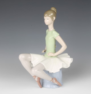 A Lladro figure of a ballet dancer sitting on a pouffe 23cm 