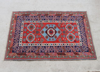 A Turkish Caucasian style red and blue ground rug with diamond shaped medallion to the centre supported by 4 small medallion within a multi row border 193cm x 133cm 