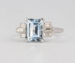 An 18ct white gold aquamarine and diamond ring, the emerald cut stone flanked by baguette cut diamonds, size N 1/2  